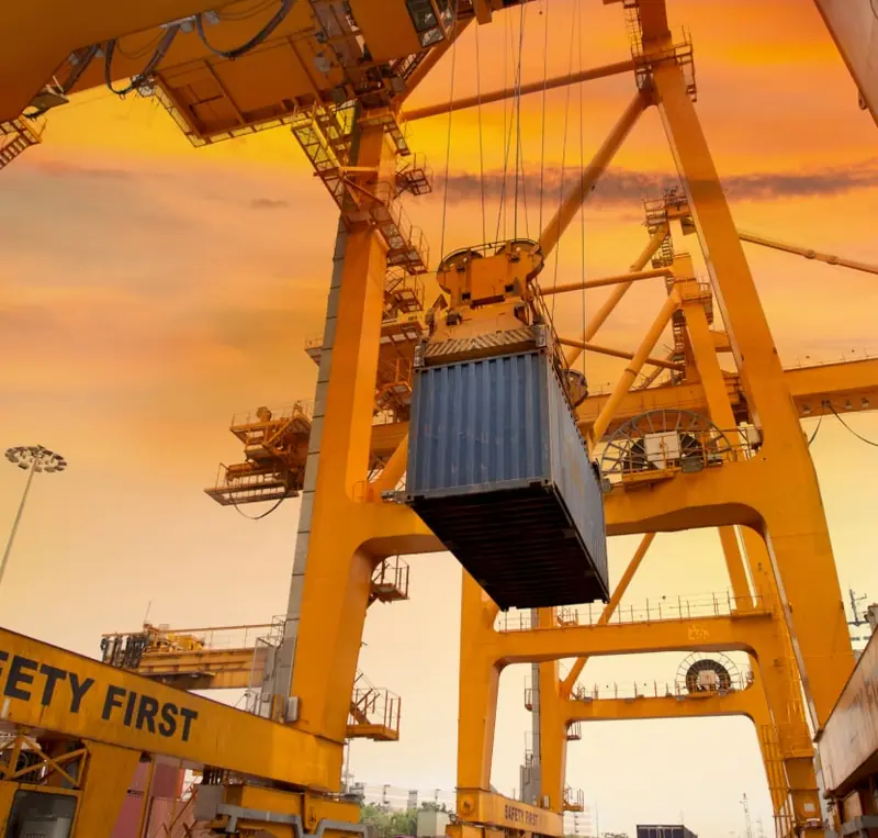 Port crane lifting a shipping container at sunset