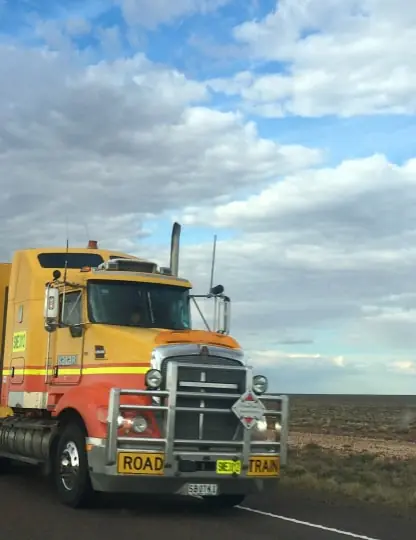Yellow semi-truck parked under a bright, cloudy sky
